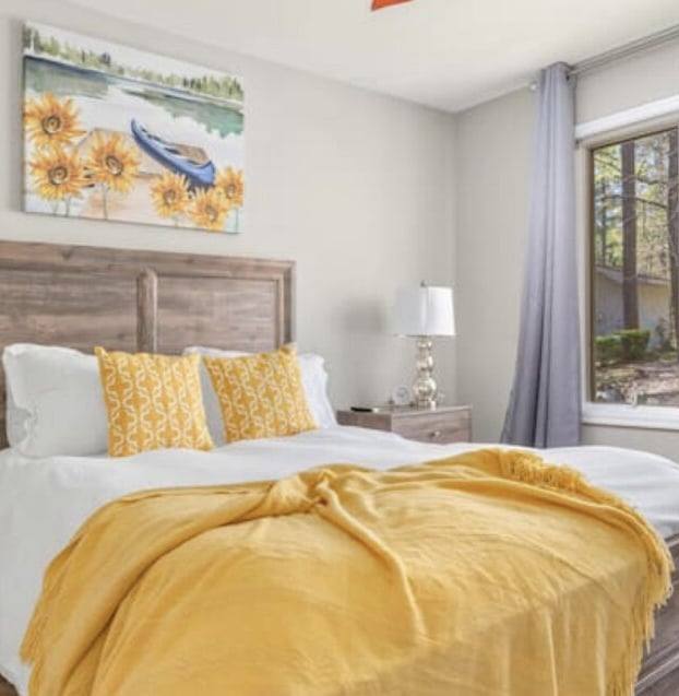 Guest bedroom with white bedding, a yellow throw and sunflower artwork