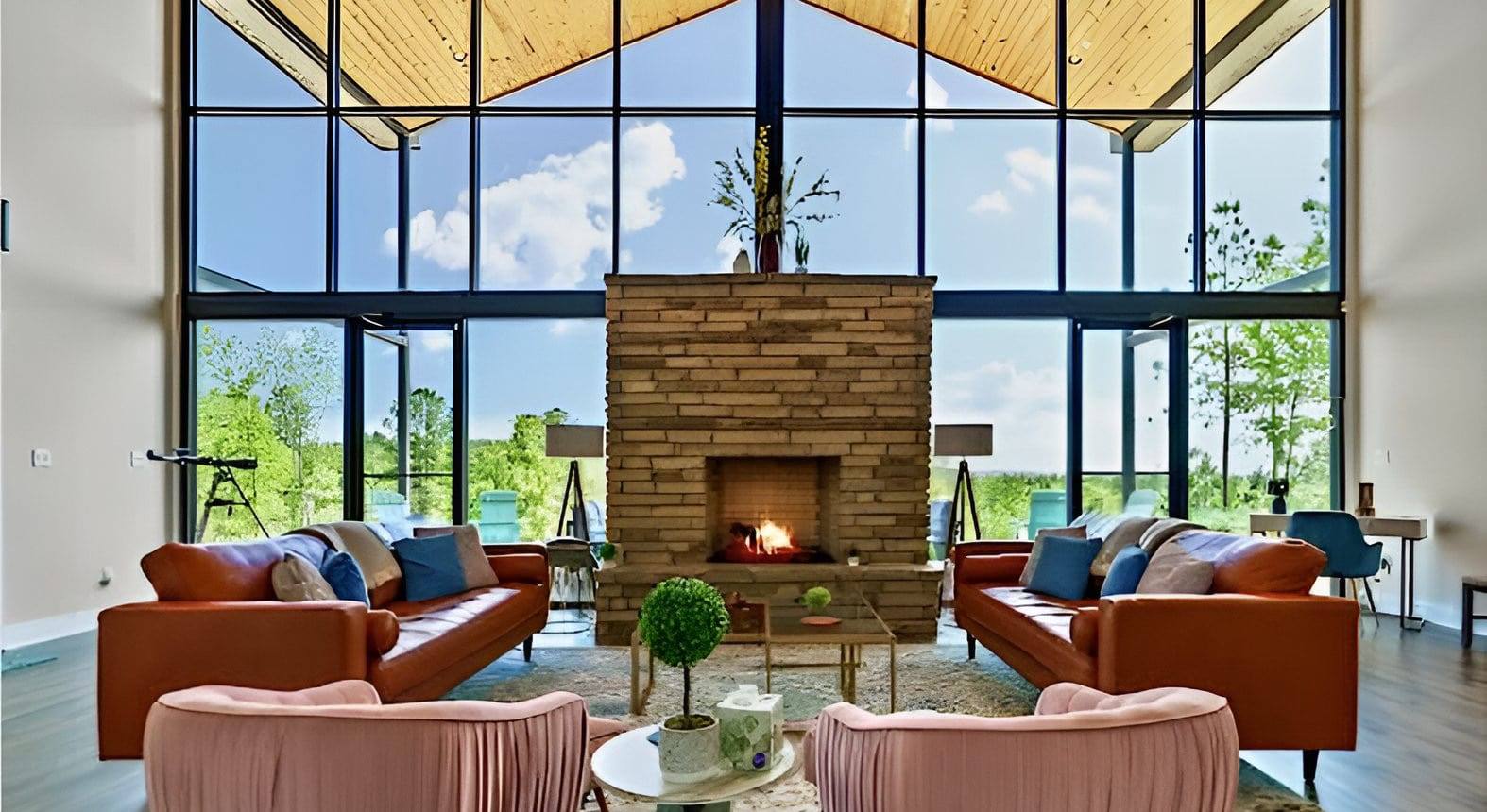 Vacation home living room with a stone fireplace, leather sofas and floor-to-ceiling windows over trees